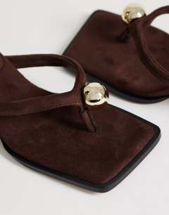 Model wearing Nadeem mid heel toe thong sandal with hardware in chocolate