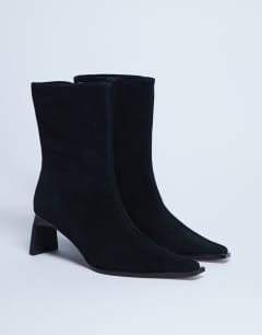 Model wearing Nadie chisel toe heeled ankle boot in black suede