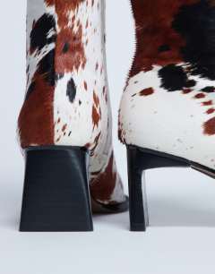 Model wearing Nadie real leather chisel toe ankle boot in cow print pony