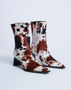 Model wearing Nadie real leather chisel toe ankle boot in cow print pony