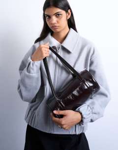 Model wearing Salma bowler bag in chocolate patent