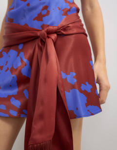 Model wearing Satin scoop neck dropped waist mini dress with fringed tie in burgundy and blue abstract print