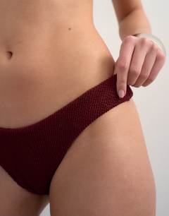 Model wearing Tara crinkle high leg cheeky bikini bottom in aubergine